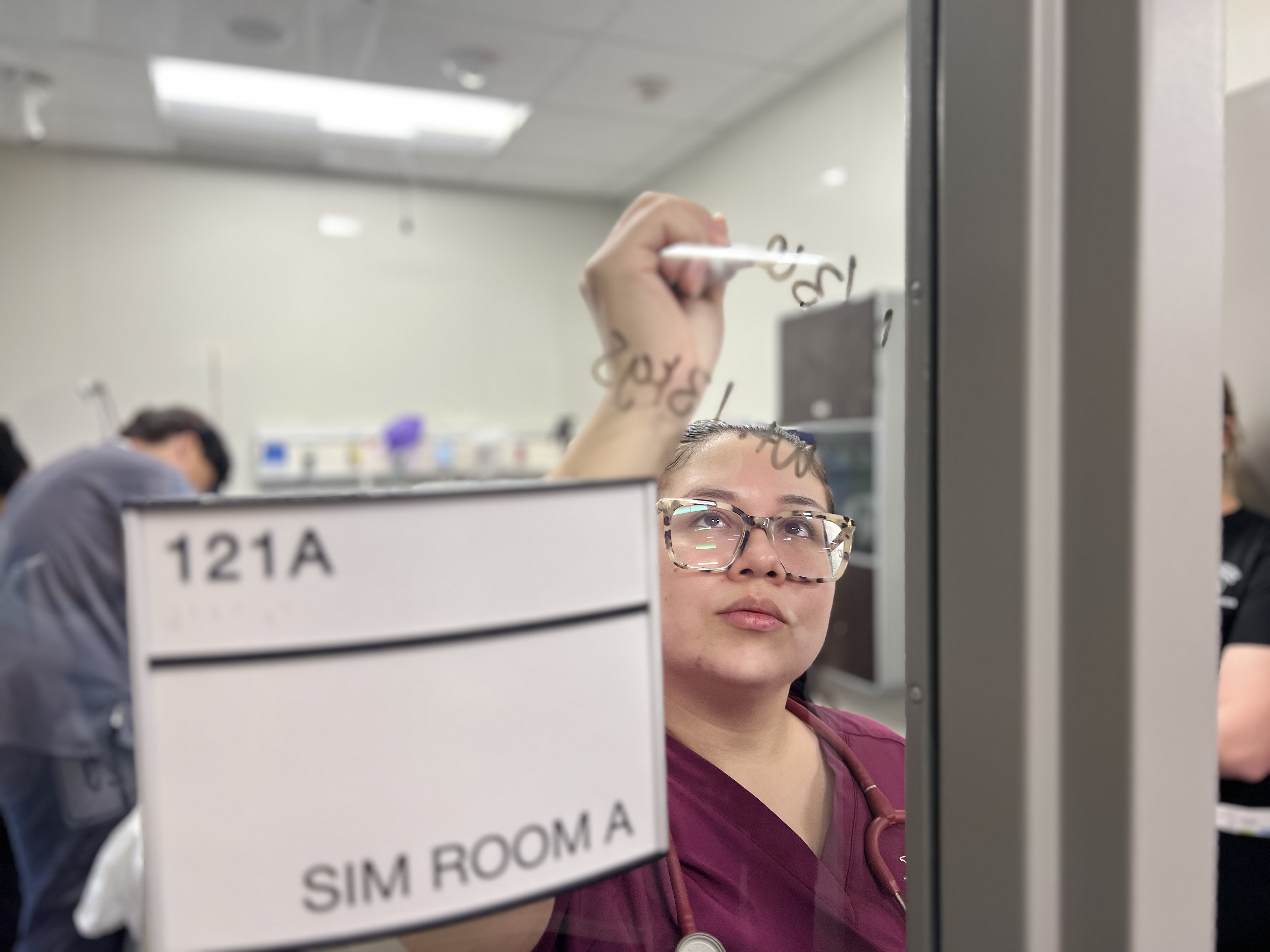 A VC nursing student writes notes on a glass door