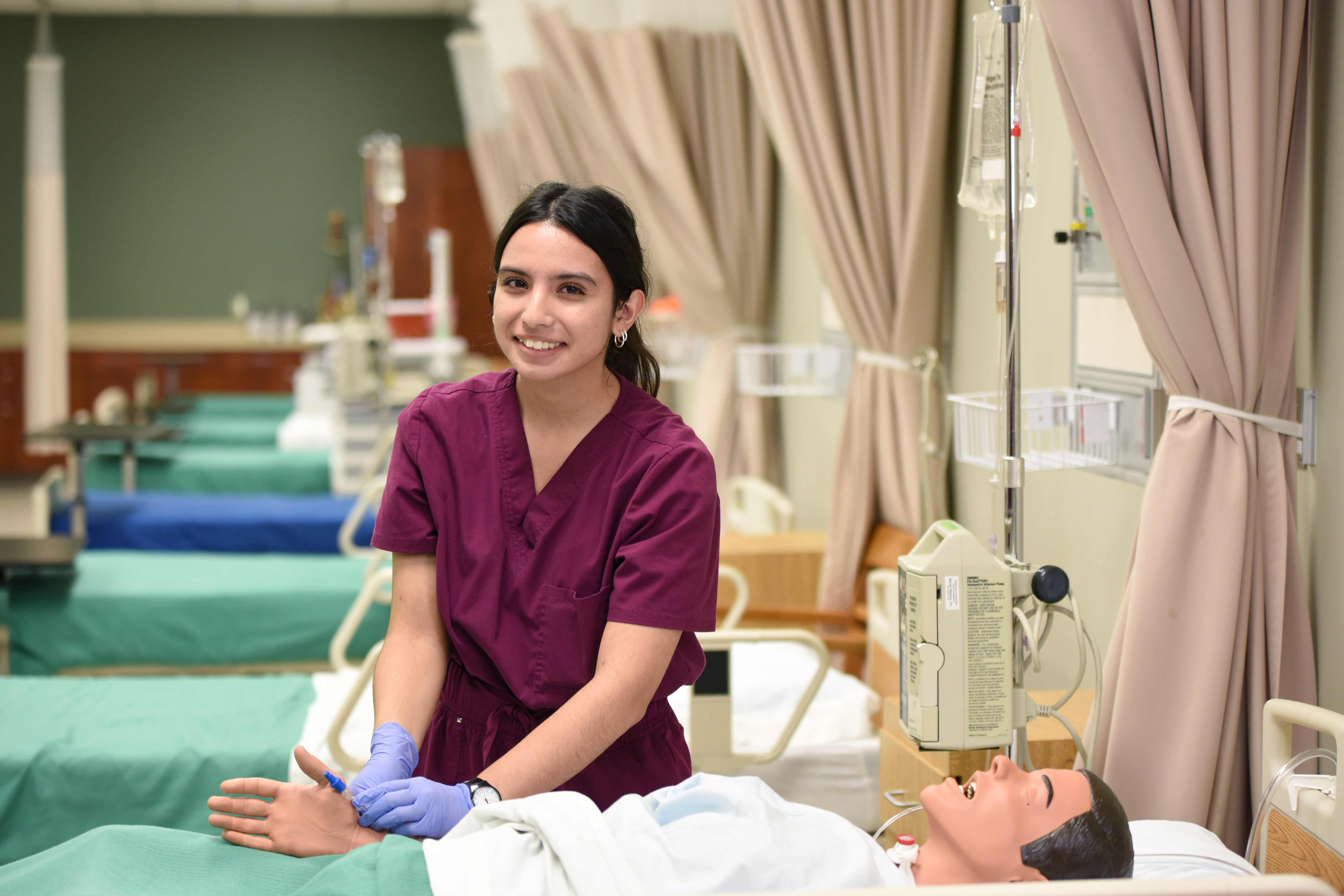 ADN student with manikin in maroon scrubs