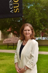 Dr Jennifer Kent in a white blazer standing beside a VC 100th anniversary banner