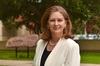 Dr Jennifer Kent in a white blazer standing beside a VC 100th anniversary banner