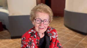 Dr Julia Riggs smiles wearing glasses and a red floral top