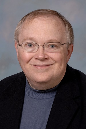 Edward Walker smiles in a black blazer on a blue background