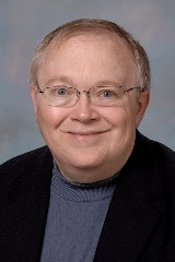 Edward Walker smiles in a black blazer on a blue background