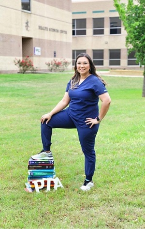 Marinda Navarro in her blue PTA scrubs with one foot up on textbooks