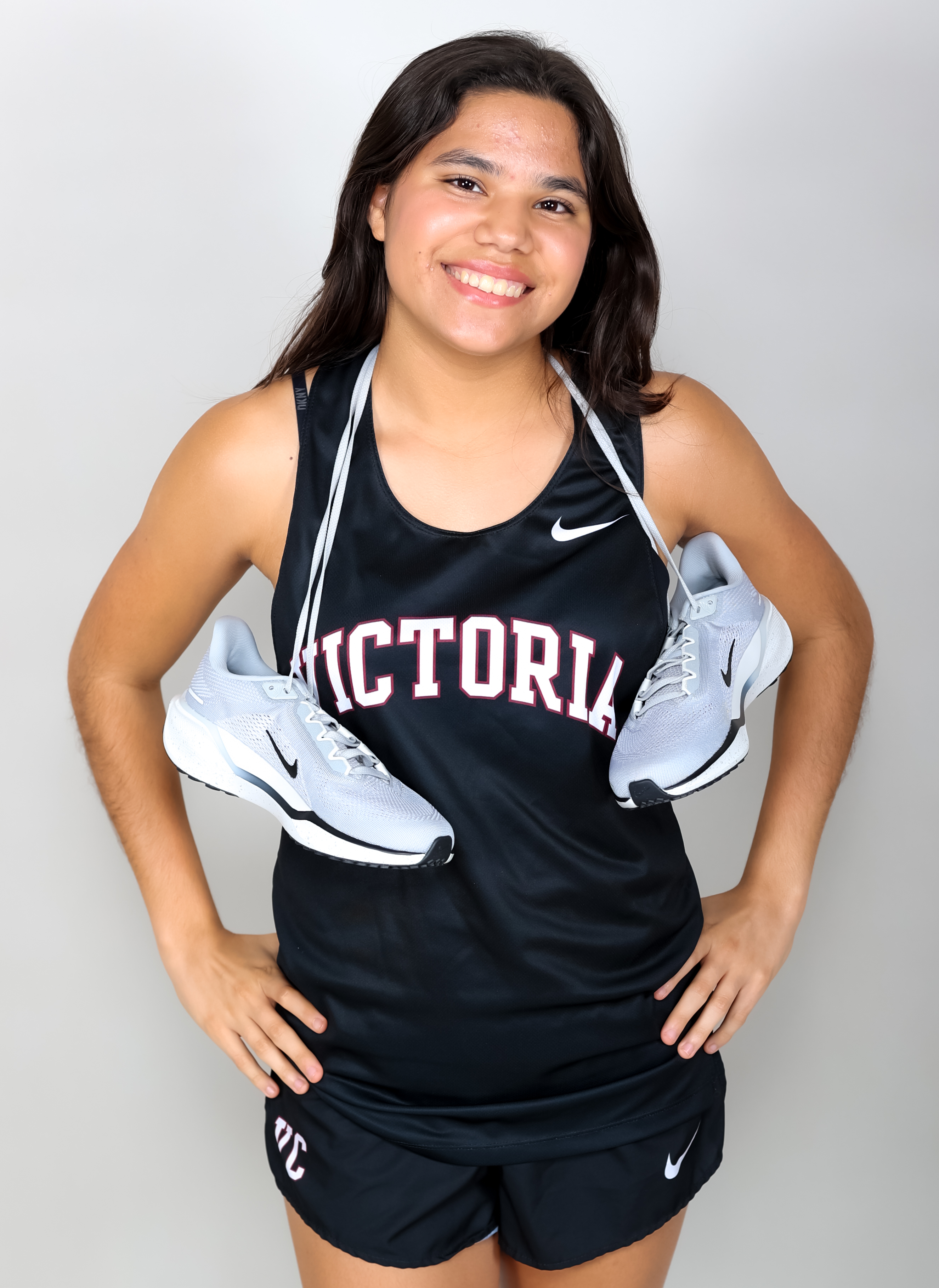 MyKenna Zarate with shoes around her neck smiles in a black VC uniform