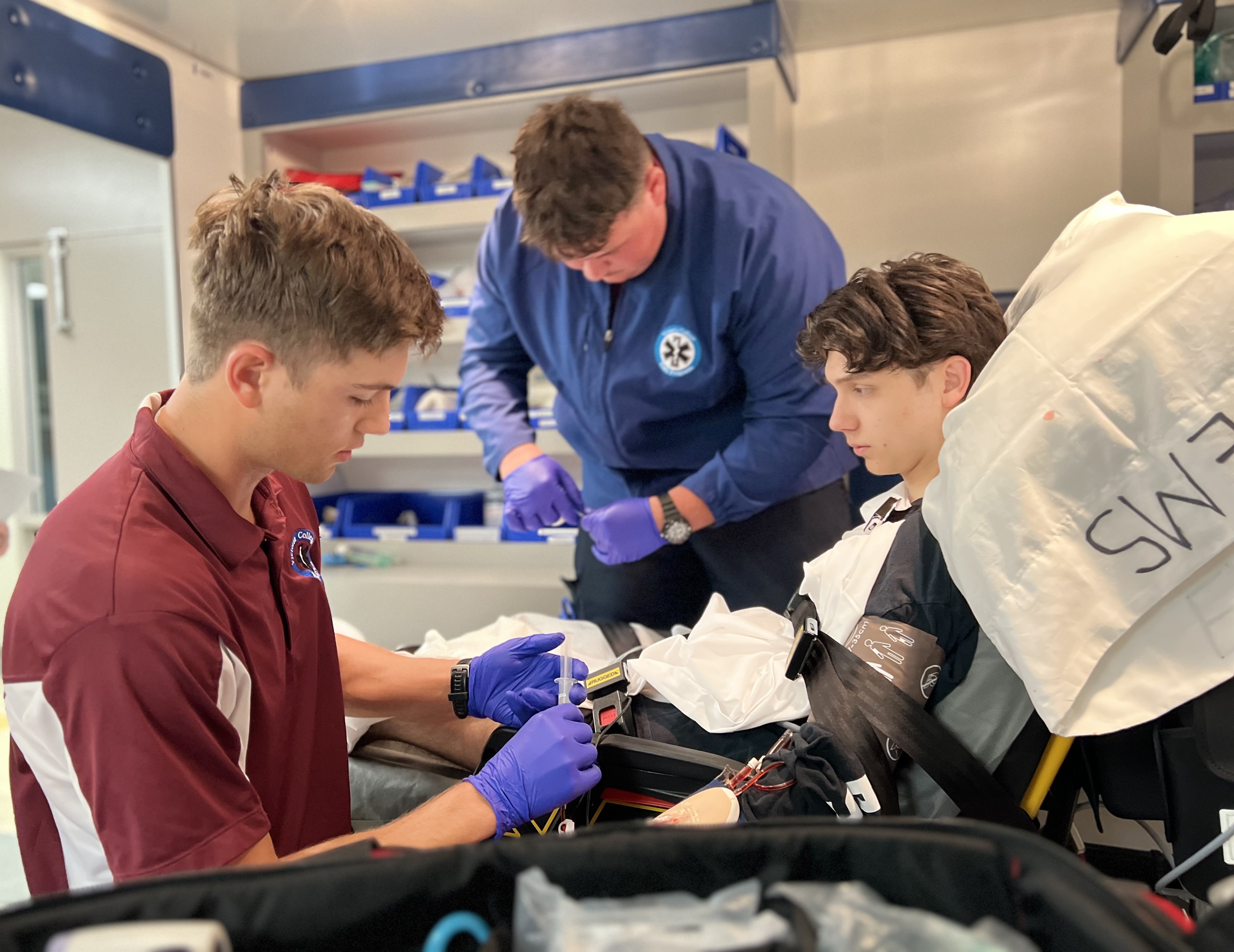 Paramedic students assist a student volunteer on a gurney