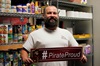 Thomas holds a #PirateProud sign inside of the Pirate Pantry with canned goods behind him