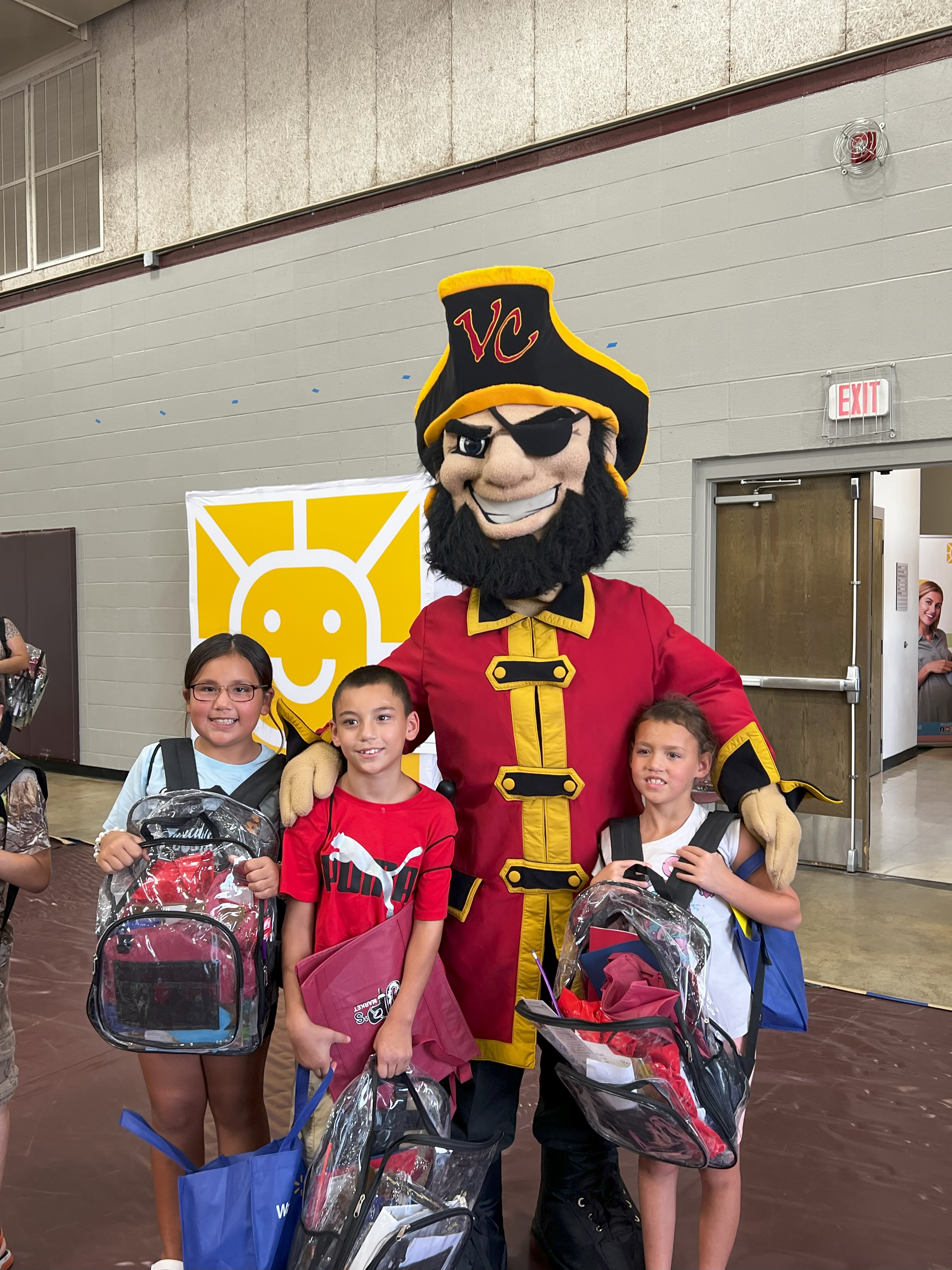 Three students hold their new backpacks next to Captain Vic