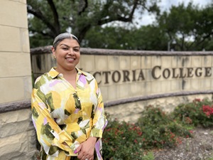 Tracy Edwards in a floral yellow dress beside a Victoria College sign